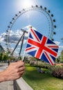 Toursist is holding flag of Great Britain in hand. London Eye in background.