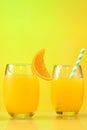 Tow glass with orange juice, half of an orange next to the glass