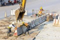 Tow man workers wear safety suits helped to lift and arrange the cement concrete barriers by stick boom arm of excavator In