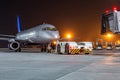Tow tractor pushes passenger aircraft from boarding bridge at night airport apron Royalty Free Stock Photo