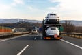 Tow truck car carrier semi trailer on highway carrying batch of new wrapped electric SUVs on motorway road at sunset