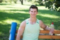 Towards healthier lifestyle. Man smiling face with yoga mat and water bottle sit on bench in park. Join outdoors yoga