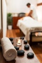 Towel, candle and lava stones in spa salon. Blurred masseur with client lying on massage table in the background Royalty Free Stock Photo