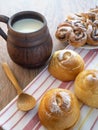 On the towel are fresh soft buns and a wooden spoon. A large mug of milk on the table Royalty Free Stock Photo