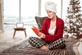 Interested restful woman in home costume sitting on bed with tablet