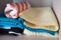 Towels on a shelf in a white cabinet. Clean ironed pink, yellow, blue towels folded in a pile. Organization of household