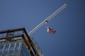 Tower Crane with an American flag near a modern office building under construction against a blue sky Royalty Free Stock Photo