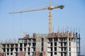 Tower crane constructing a new residential building at a construction site against blue sky. Renovation program, development, Royalty Free Stock Photo