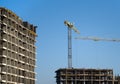 Tower crane constructing a new residential building at a construction site against blue sky. Renovation program, development, Royalty Free Stock Photo