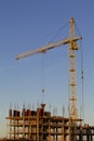 Tower crane on the construction of a building with a frame of reinforced concrete. Flooded by the light of the setting sun. Royalty Free Stock Photo