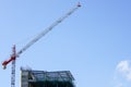 Tower crane and a fragment of the facade of an unfinished building on blue sky background Royalty Free Stock Photo