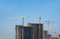 Tower cranes constructing a new residential building at a construction site against blue sky. Renovation program, development, Royalty Free Stock Photo