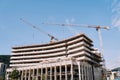 Tower cranes work at the construction site of a multi-storey building against a cloudy sky