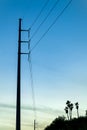 Towering power lines and poles in sillhouette lighting with blue and white sky and orange sunrise with palm trees nature Royalty Free Stock Photo