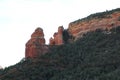 Towering Red Sandstone Rock Formation And Sheer Cliff Leading To Sloping Canyon Walls Filled With Evergreen Trees