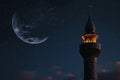 A towering structure with an illuminated beacon at its peak, standing tall against the sky, A crescent moon over a mosque\'s