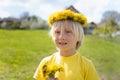 Towheaded boy wears wreath of flowers and holds bouquet of dandelions standing in meadow. Summer vacation time