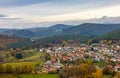 a town nestled in the mountains surrounded by trees and grass with a cloudy sky above it and a few sheep grazing in the foreground