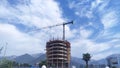 In a town surrounded by a mountain range, a high-rise round concrete building is being erected by a crane among residential houses Royalty Free Stock Photo