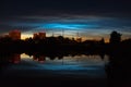 Town view of noctilucent clouds NLC. Beautiful waves and ripples of silver blue night shining clouds over some houses in summer