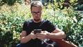 Man is browsing social nets by his smartphone outdoors in park, sit on bench