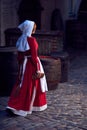 Townswoman in red dress with an apron and chaperone on the street.