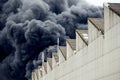 Black plumes of smoke from an accidental toxic industrial fire as seen from a behind a factory building.