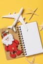 Toy airplane, Santa Claus and notebook on a yellow background with copy space. Christmas travel planning concept