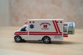 A toy ambulance on a wooden table with a rolled up one hundred American dollar bill in the back. High prices for ambulance Royalty Free Stock Photo