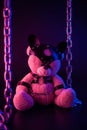 Toy bear dressed in leather belts harness accessory for BDSM games on a dark background in neon light