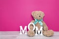 Toy bear with letters MOM on fuchsia background.