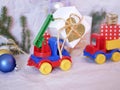 Toy bright cars deliver boxes with gifts, Christmas decorations, New Year`s decor, balls on a light background