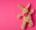toy brown plush hare lies on a pink background