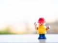 Toy builder worker with red helmet with two hands up in blurry background. Mini figure construction with copy space