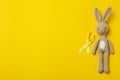 Toy bunny and child cancer awareness ribbon on yellow background