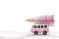 Toy bus car carries a Christmas tree from the forest. Pink and white colors, winter holiday new year mood Royalty Free Stock Photo