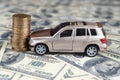 Toy car in accident on a background of 100 dollar bills and stack of golden coins