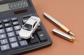 Toy car, calculator and pen on a brown background. Car rental, purchase or insurance. Royalty Free Stock Photo