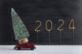 Toy car carries miniature Christmas tree, golden number 2024 on black background. Delivery of Christmas trees concept