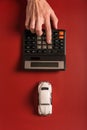 Toy car and hand counting on a calculator on a maroon background, the concept of selling and buying a car Royalty Free Stock Photo