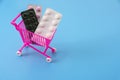 A toy cart from the supermarket with multicolored blisters with pills on a blue background