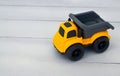 Toy childrens dump truck on a white wooden background.Yellow and grey miniature car. Royalty Free Stock Photo