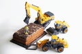 Toy construction machinery and a worker with a jackhammer next to a piece of chocolate cake. The concept of construction,