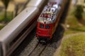 A toy electric train with a train train passes by a road with cars. Royalty Free Stock Photo