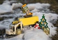 Toy excavators, a yellow wagon, a souvenir snowman, golden gifts stand in snow