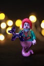 Toy female genie figure with red hair and lips holding a purple balloon animal