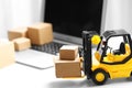 Toy forklift with boxes near laptop. Logistics and wholesale concept