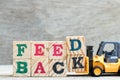 Toy forklift hold letter block d,k to word feedback on wood background