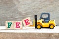 Toy forklift hold letter block e to word fee on wood background