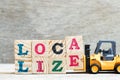 Toy forklift hold letter block a.e to word localize on wood background Royalty Free Stock Photo